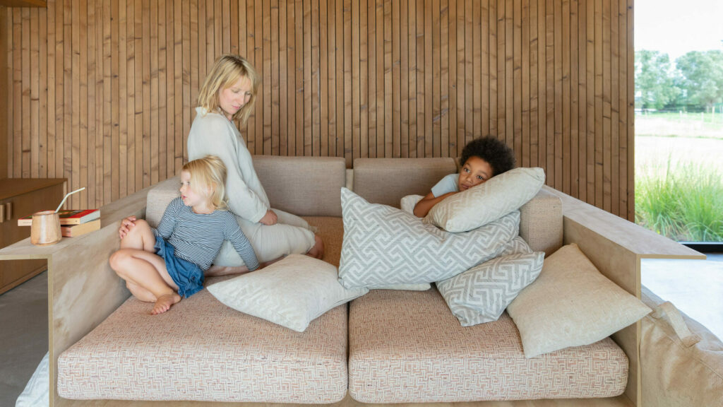 two girls and their mom lounge and play on an elegantly oversized neutral sofa in a japandi style living room