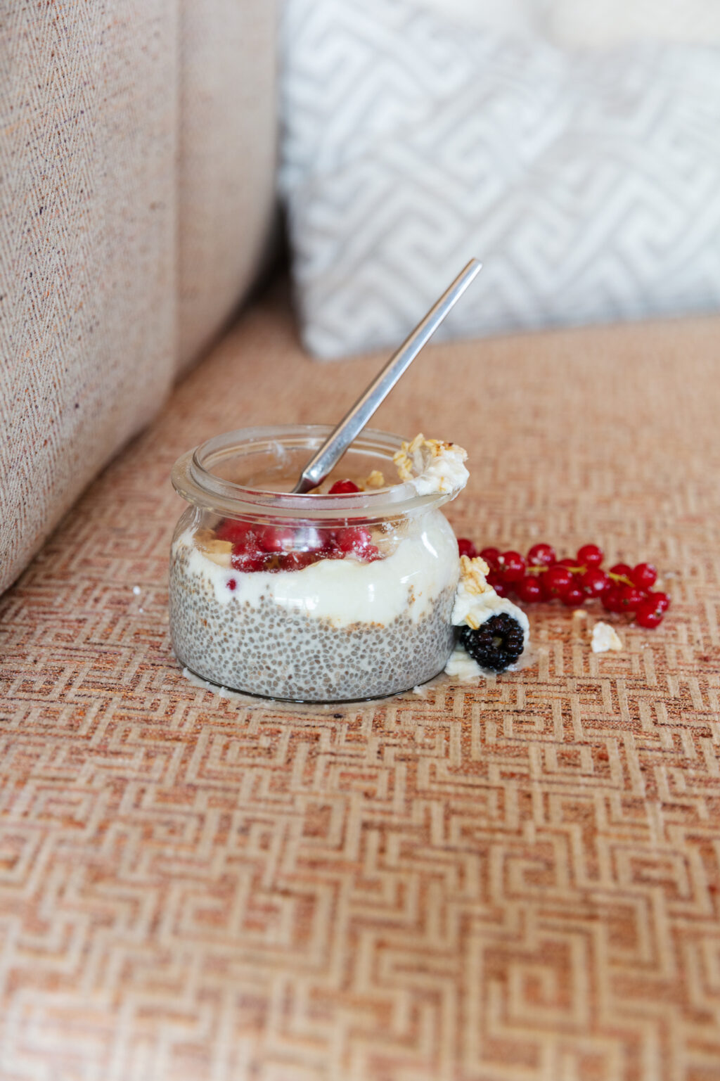 a jar of breakfast yogurt and fresh berries spills out onto a geometric patterned sofa fabric