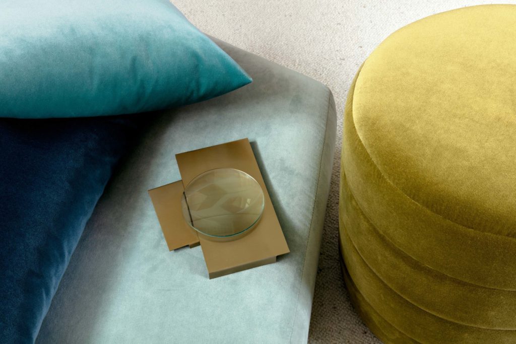 closeup of teal performance velvet sofa with teal coloured pillow and a round yellow ottoman